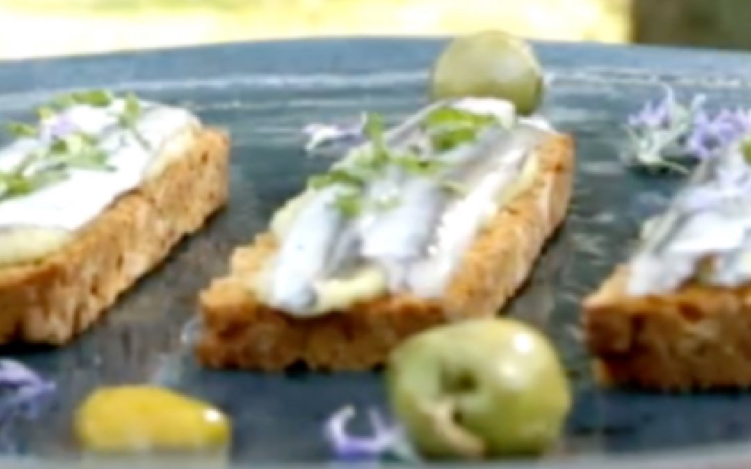 Boquerones marinados en cítricos sobre tostas de pan de tomate y hummus de aceituna Manzanilla